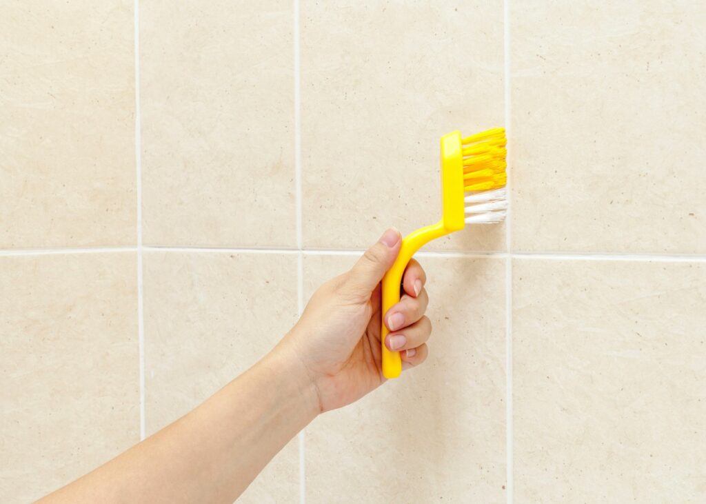 Person using brush to clean shower tiles