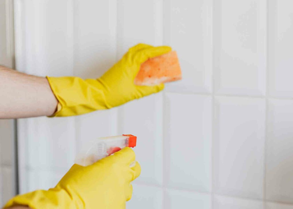 Person with gloves and cleaning equipment cleaning shower tiles